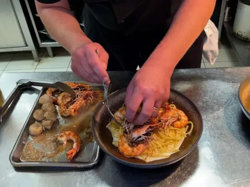 Un chef prépare des pâtes aux crevettes et pétoncles, un plat savoureux de cuisine de terroir.
