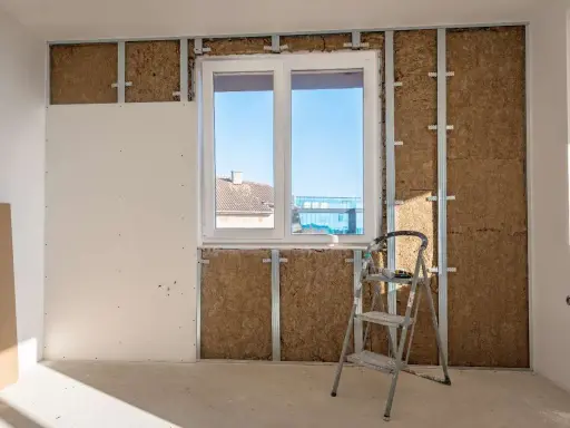 Instalación de un trasdosado de pladur con aislamiento, mostrando la estructura metálica, la lana de roca y una placa de yeso.