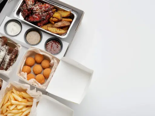 Variedad de comida para llevar: alitas, costillas, papas fritas, croquetas y pan. ¡Todo listo para disfrutar!