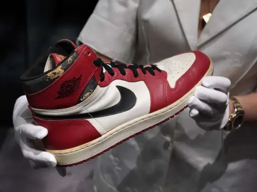 Ein Paar abgenutzte Air Jordan 1 Sneaker, die seit 1985 erhältlich sind, werden von einer Person mit weißen Handschuhen gehalten.