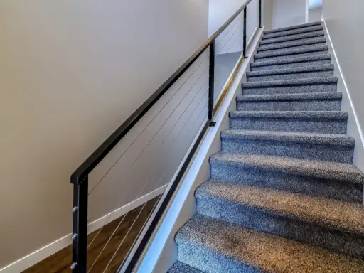 Miękka wykładzina na schody betonowe zapewnia komfort i bezpieczeństwo. Nowoczesna balustrada z linkami dodaje elegancji.