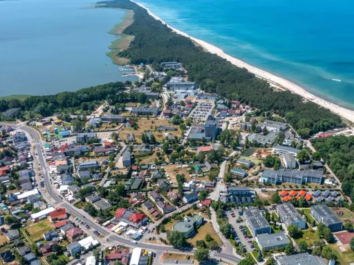 Dąbki atrakcje: widok z lotu ptaka na nadmorską miejscowość z jeziorem, plażą, lasem i zabudowaniami.
