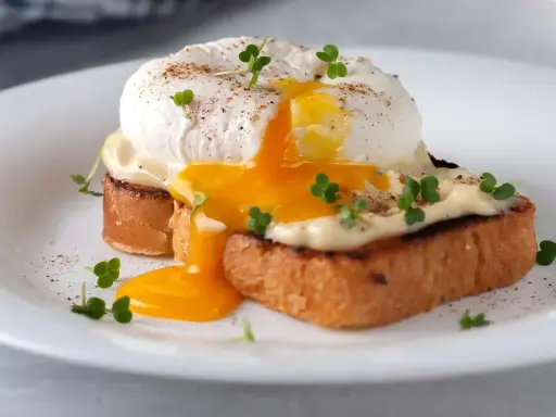 Un delicioso huevo poche con yema líquida cayendo sobre tostadas, adornado con brotes verdes y pimienta.