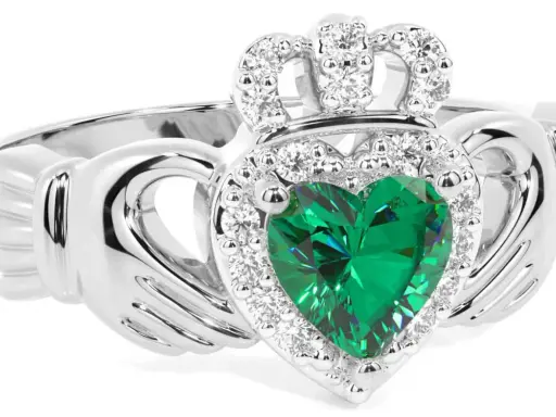 Anello Claddagh con cuore verde smeraldo, circondato da diamanti e sormontato da una corona scintillante.