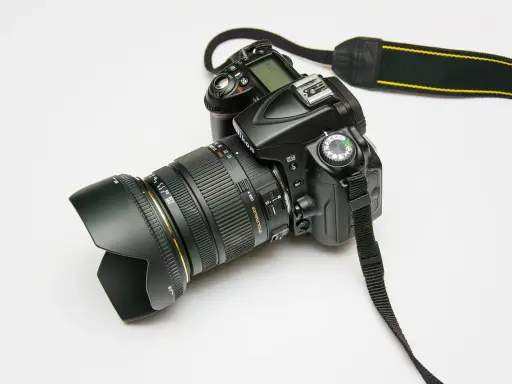 Czarny aparat fotograficzny z obiektywem i paskiem na białym tle.