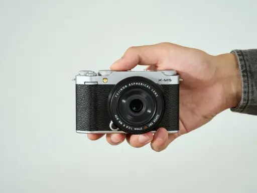 Mano sujetando una cámara Fujifilm X-M5 plateada y negra, lista para capturar momentos.