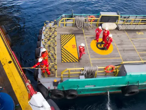 Équipage en combinaison rouge ajustant la longueur du bout de remorquage du bateau. Ils travaillent sur le pont d'un navire, manœuvrant une corde.