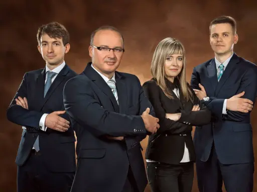 Cztery osoby w garniturach stojące z rękami skrzyżowanymi na piersi.