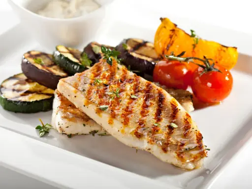Gebratener Seelachs mit gegrilltem Gemüse wie Zucchini, Aubergine und Tomaten, garniert mit Kräutern.