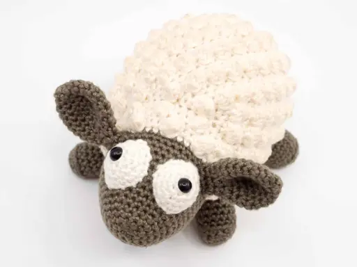 Oveja amigurumi de ganchillo con lana crema y marrón, ojos grandes y expresivos, lista para abrazar.