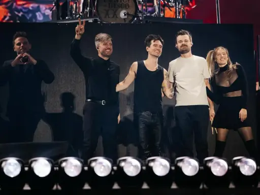 Medlemmar av Panic! at the Disco på scenen, en gör hjärta med händerna, en annan vinkar med två fingrar.