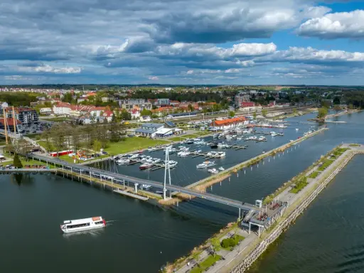 Widok na port w Giżycku, gdzie cumują liczne jachty i statki. Nowoczesny most pieszy łączy brzegi, a w tle rozciąga się miasto. To idealne miejsce na odkrywanie giżycko atrakcje.