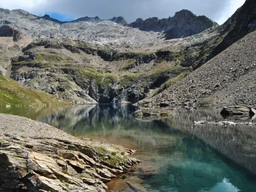 Riflessi perfetti sul lago nero, incastonato tra montagne rocciose e verdi pendii.