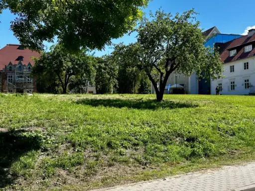 Zielona polana przed zabytkowymi budynkami, idealne miejsce na relaks i odkrywanie sztynort atrakcje.