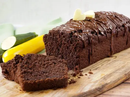 Saftiger schokokuchen mit zucchini, überzogen mit Schokoladenglasur und garniert mit zwei kleinen Herzchen aus hellem Teig.