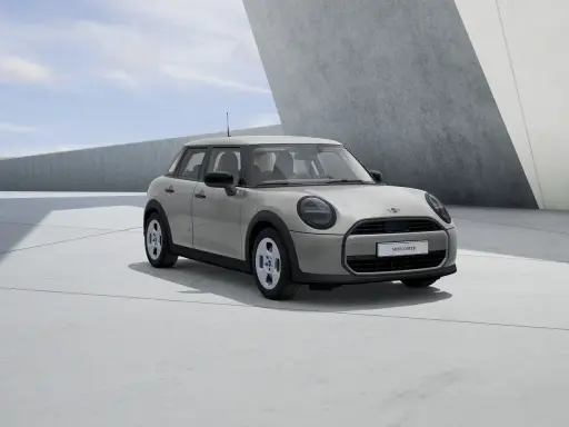 Mini Cooper 5 puertas en color gris claro, con llantas plateadas, estacionado en una zona de concreto con arquitectura moderna.