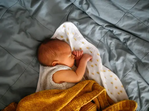 Noworodek śpi otulony kocykiem. Skóra dziecka ma lekko żółtawy odcień, co może sugerować żółtaczkę u dziecka.