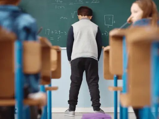 Chłopiec stoi przed tablicą z zadaniami matematycznymi.