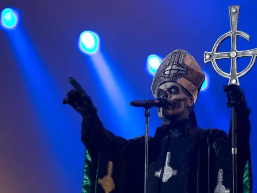 Jocke Berg som Papa Emeritus IV från Ghost, med vit ansiktsmålning och en korsstav, pekar mot publiken under en konsert.