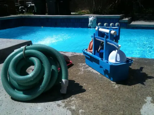 Un tuyau vert enroulé et une boîte bleue avec des accessoires de piscine, prêts pour le nettoyage. L'ordre des filtres à eau est essentiel pour une eau claire.
