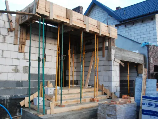 Budowa domu w toku. Drewniana konstrukcja stropu podtrzymywana przez liczne metalowe podpory.
