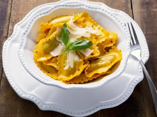 Un piatto invitante di tortelli di zucca, guarniti con scaglie di parmigiano e una fogliolina di basilico, pronti per essere gustati.