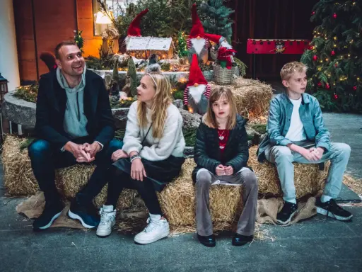 Familj njuter av en mysig stund vid en juldekoration med tomtar och gran. En härlig svensk julkänsla.