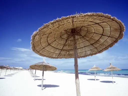 Pusta plaża w Tunezji, słomiane parasole i błękitne niebo. Idealna pogoda w listopadzie na spokojny wypoczynek.