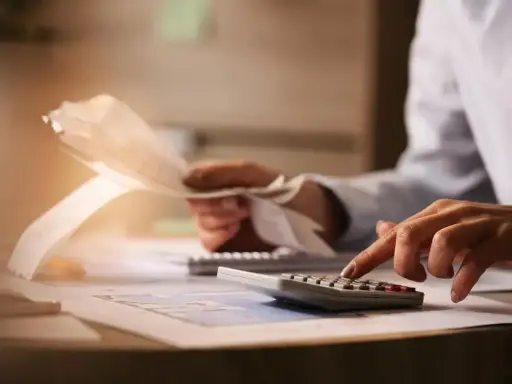 Manos calculando gastos y revisando recibos. Planificar el futuro financiero, como un plan de pensiones, merece la pena.