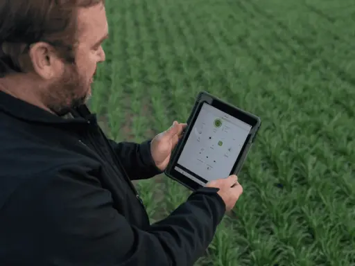Farmer uses a tablet to monitor crop health and optimize yields, showcasing the power of digital farming in a lush green field.