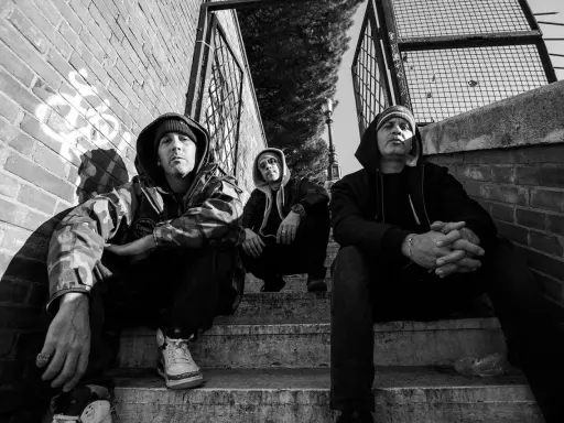 Tre uomini con cappuccio siedono sulle scale, un'atmosfera da musica hip hop famosa.