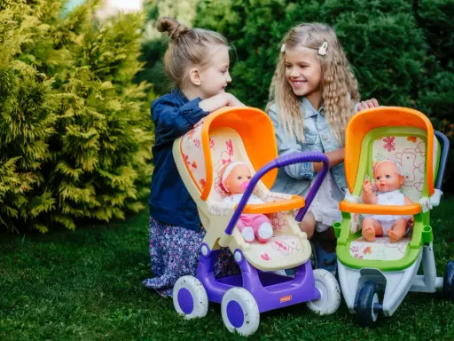 Dwie dziewczynki bawią się lalkami w wózkach, odgrywając różne etapy życia dziecka.