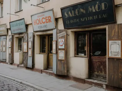 Ulica w dzielnicy żydowskiej Krakowa z zabytkowymi szyldami sklepów: "Salon Mód", "Benjamin Holcer Stolaz", "Stanisław Nowak Sklep Spożywczy".