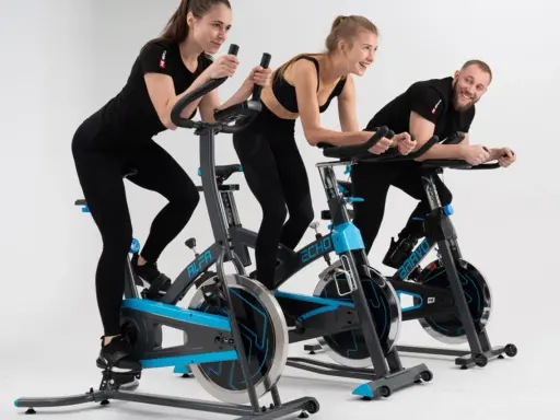 Trzy osoby ćwiczą na rowerach stacjonarnych. To świetny trening spinningowy!