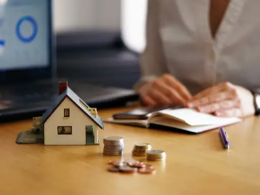 Maqueta de casa, monedas y portátil con gráfico. Persona anotando en libreta. Analizando el precio vivienda.