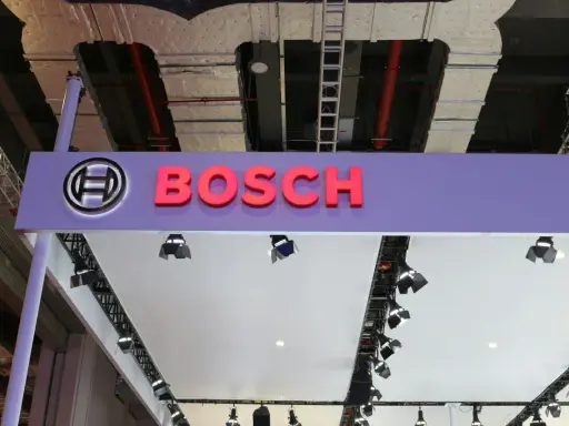 Logo Bosch i nazwa firmy na fioletowym tle. W tle widać instalacje przemysłowe, przewody i drabiny, sugerujące miejsce, gdzie odbywa się produkcja.