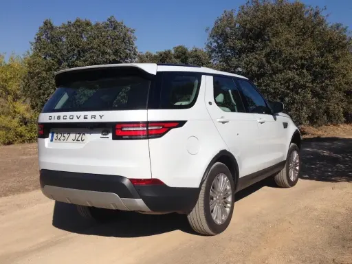 Un Land Rover Discovery HSE blanco aparcado en un camino de tierra rodeado de árboles.