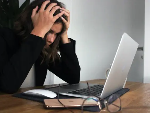 Kobieta z rękami na głowie przy laptopie, symbolizująca wypalenie i decyzję o porzuceniu pracy.
