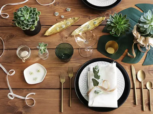 En vacker dukning med suckulenter, gyllene detaljer och gröna blad. En inbjudande och stilren bordsuppsättning.