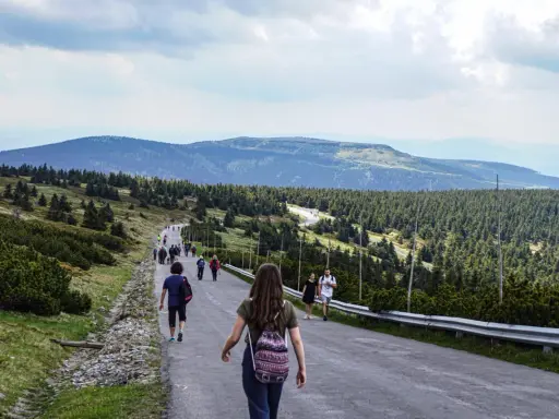 Grupa turystów wędruje pod górę w kierunku pradziad szczyt. W oddali widać pasma górskie i lasy.
