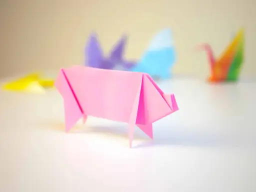 Cerdo de origami rosa con otras figuras de papiroflexia desenfocadas al fondo.