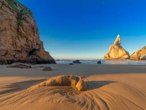 Goldene Sanddünen und Felsen am Praia da Ursa im warmen Abendlicht.