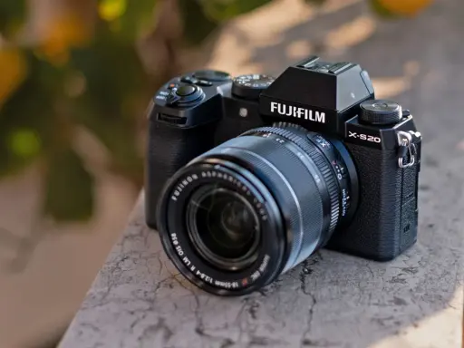 Czarny aparat Fujifilm X-S20 z obiektywem Fujinon leży na kamiennym murku.