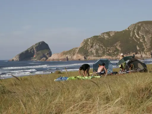 Gente en un playón de bayas, con carpas y sombrillas, disfrutando del mar y las montañas.