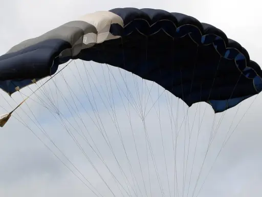 Ein großer, mehrfarbiger Fallschirm öffnet sich im Himmel, bereit für den Sprung aus dem Flugzeug.