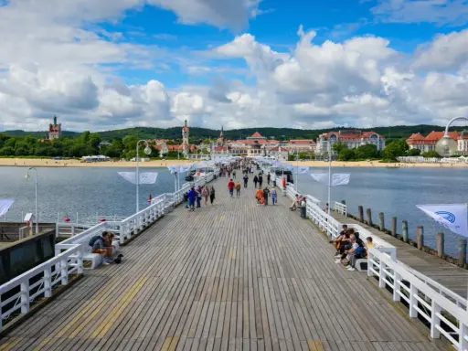 Spacer w Sopocie tętni życiem. Ludzie spacerują po drewnianym molo, podziwiając widok na plażę i zabytkowe budynki.
