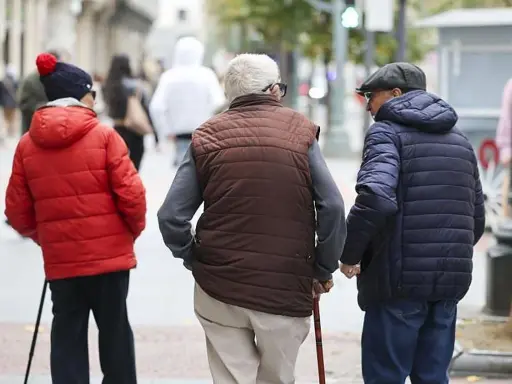 Tres personas mayores caminan por la calle, una con bastón, reflexionando sobre la **pensión mínima**.