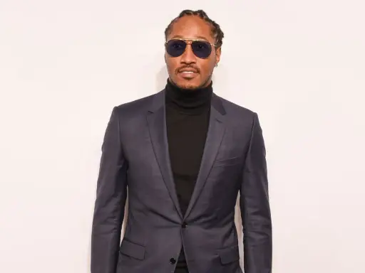 A man in a sharp black suit with a turtleneck, sporting stylish sunglasses.