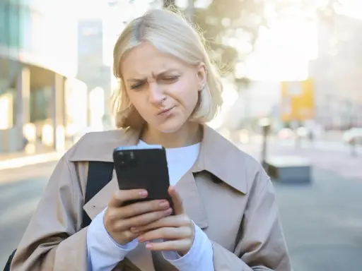 Zmarszczona kobieta patrzy na telefon, zastanawiając się, jak przestać zazdrościć innym.