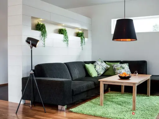 Ett modernt vardagsrum med mörk soffa, gröna kuddar och en träbord. Ljus och rum skapar en inbjudande atmosfär med växter i en nisch.